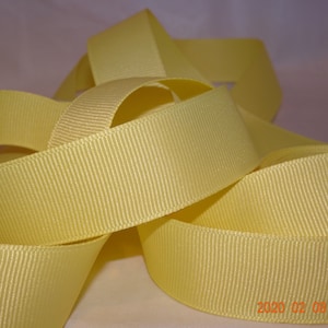 May include: A close-up of a yellow satin ribbon. The ribbon is folded and arranged in a decorative way. The ribbon has a subtle sheen and a smooth texture.