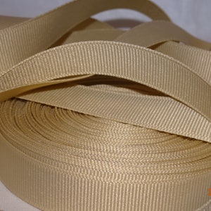 May include: A roll of beige grosgrain ribbon. The ribbon is folded and rolled up, showing the texture of the fabric.