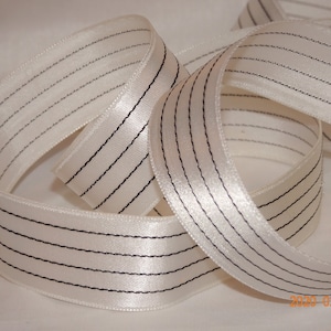 May include: White satin ribbon with black stitched stripes. The ribbon is approximately 2.5 cm wide.