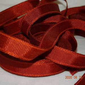 May include: A close-up of a spool of rust-colored grosgrain ribbon. The ribbon is woven with a textured, ribbed pattern.