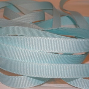 Könnte beinhalten: Nahaufnahme eines hellblauen Satinbandes. Das Band ist gefaltet und verdreht, wodurch seine Textur und sein Glanz sichtbar werden.