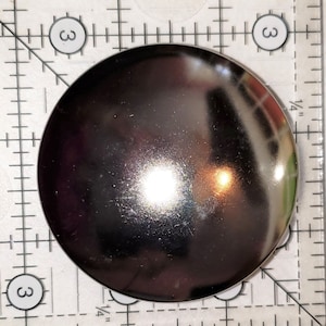 May include: A round, silver-colored metal button with a smooth, shiny surface.