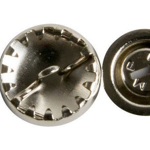 May include: A silver metal button with a decorative edge and a small metal loop on the top. The back of the button has a circular design with the letters "F.R.A." inside.
