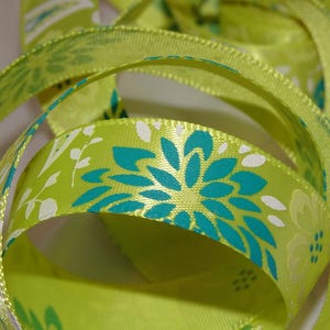 Puede incluir: Cinta de satén verde con un patrón floral blanco y turquesa. La cinta está doblada y retorcida, mostrando el patrón desde diferentes ángulos.