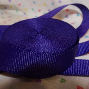 Könnte beinhalten: Eine Rolle tiefes, violettes Satinband. Das Band ist in der Mitte gefaltet und die Enden sind eingerollt.