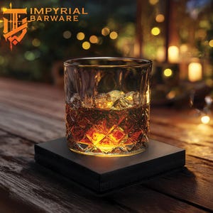 May include: A clear, diamond-cut whiskey glass filled with amber liquid and ice cubes, resting on a black square base. The glass is illuminated from below, creating a warm glow. The logo "IMPYRIAL BARWARE" is visible in the top left corner.
