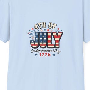 May include: Light blue t-shirt with a graphic that says "4th of July Independence Day 1776" in red, white, and blue. The shirt is a crew neck and has short sleeves.
