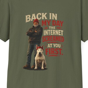 Könnte beinhalten: Ein olivgrünes Kurzarm-T-Shirt mit einer Grafik einer Person und eines Hundes, die rote Mützen tragen. Der Text lautet: BACK IN MY DAY THE INTERNET SCREAMED AT YOU FIRST. Das Design ist mittig auf der Brust des Rundhals-T-Shirts platziert.