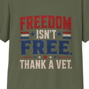 May include: Olive green t-shirt with the text "FREEDOM ISN'T FREE. THANK A VET." in red, white, and blue lettering. The design features stars and stripes, evoking a patriotic theme. The shirt is a classic crew neck style.
