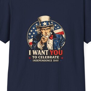 May include: Navy blue t-shirt featuring a graphic of Uncle Sam pointing, with the text "I WANT YOU to celebrate Independence Day." The design includes red, white, and blue colors, and a star-studded background.