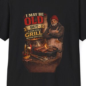 Puede incluir: Camiseta negra con un gráfico de un hombre a la parrilla. El texto dice "I MAY BE OLD BUT I CAN STILL GRILL BETTER THAN YOU." El hombre lleva un gorro rojo y un delantal. Una parrilla con comida está en primer plano.