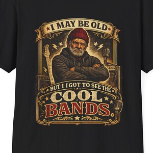 May include: Black t-shirt featuring a vintage-style graphic. The graphic includes the text "I MAY BE OLD BUT I GOT TO SEE THE COOL BANDS" with an illustration of a man in a beanie, guitar, and microphone.