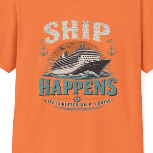 May include: Orange t-shirt with a graphic of a cruise ship on the ocean, the words "SHIP HAPPENS" and "LIFE IS BETTER ON A CRUISE". The design includes anchors and a stylized wave.
