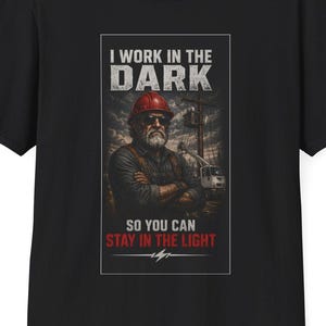 May include: Black t-shirt with a graphic of a construction worker in a red hard hat. The text on the shirt reads "I WORK IN THE DARK SO YOU CAN STAY IN THE LIGHT."