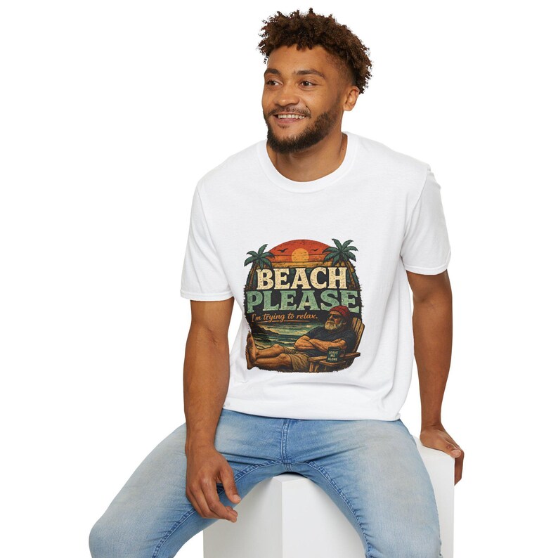 A smiling man wearing a white t-shirt with a graphic design of a beach scene and the text "BEACH PLEASE" is sitting on a white stool.