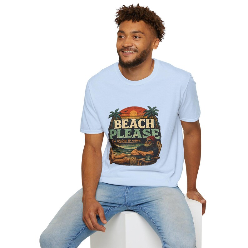 A smiling man wearing a white t-shirt with a graphic design of a beach scene and the text "BEACH PLEASE" is sitting on a white stool.