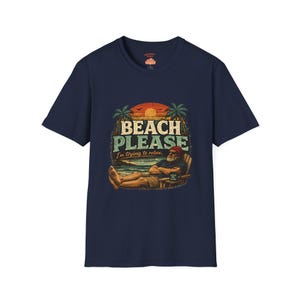 A navy blue t-shirt with a graphic design depicting a man relaxing on a beach, with the text "BEACH PLEASE I'M DYING TO RELAX" printed on it.