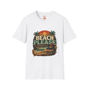 A white t-shirt with a graphic design featuring a man relaxing on a beach chair with palm trees and a sunset in the background.
