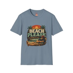 A t-shirt with a graphic design featuring a man relaxing on a beach chair with palm trees and a sunset in the background. The text on the t-shirt says "BEACH PLEASE I'M DYING TO RELAX".