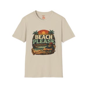 A t-shirt with a graphic design featuring a man relaxing on a beach with palm trees and a sunset in the background. The text on the t-shirt says "BEACH PLEASE I'M DYING TO RELAX".