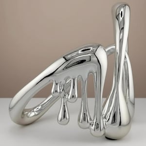 Puede incluir: Una escultura abstracta moderna con un acabado plateado pulido. La obra de arte presenta formas orgánicas fluidas que parecen derretirse o gotear. La escultura tiene una superficie reflectante, creando un efecto visual dinámico.