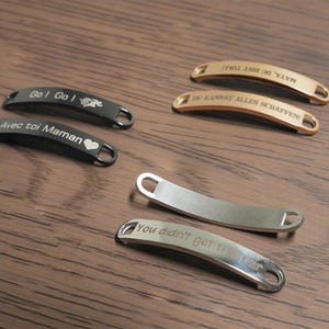May include: A collection of engraved metal tags in various colors, including black, silver, and gold. The tags have curved designs with text such as "Go! Go!" and "You didn't get this far."