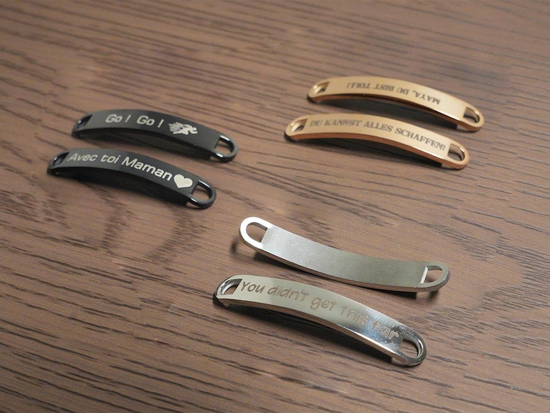 May include: A collection of engraved metal tags in various colors, including black, silver, and gold. The tags have curved designs with text such as "Go! Go!" and "You didn't get this far."