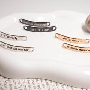 May include: A collection of curved metal tags with engraved text. Some tags are silver, others are gold or black. The text includes phrases like "I'm feeling", "You didn't get this far", and "Go! Go!".