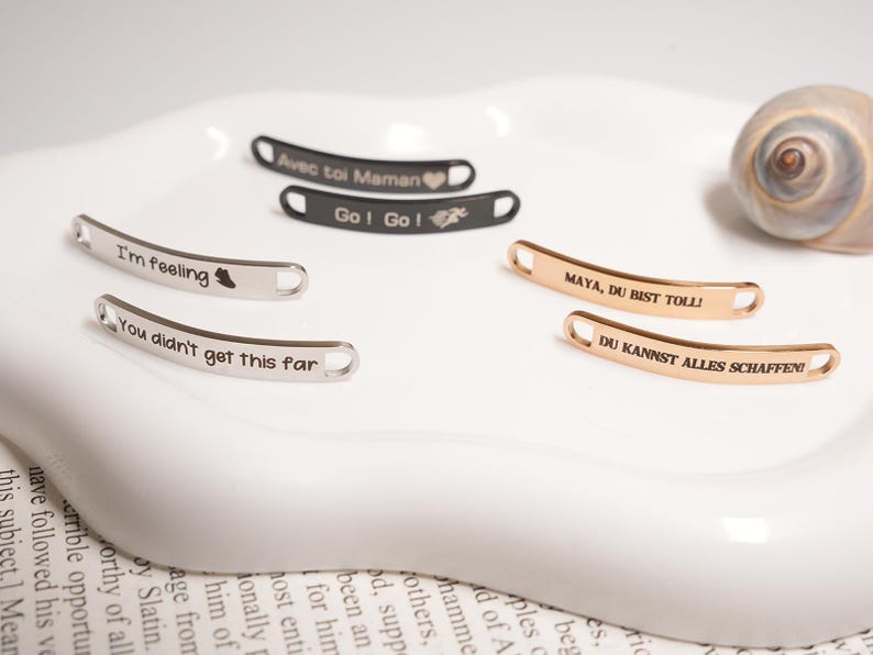 May include: A collection of curved metal tags with engraved text. Some tags are silver, others are gold or black. The text includes phrases like "I'm feeling", "You didn't get this far", and "Go! Go!".