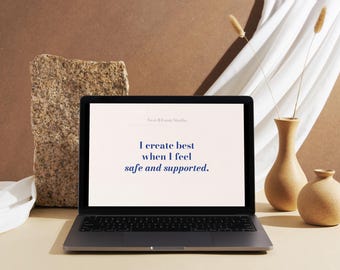 May include: A laptop displays the text "I create best when I feel safe and supported." The laptop is open on a light-colored surface, with a stone block and two vases in the background. The vases are beige and hold dried plants.