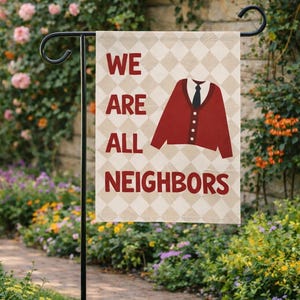 May include: A garden flag with the words "WE ARE ALL NEIGHBORS" in burgundy letters. The flag features a burgundy cardigan and tie graphic on a beige diamond pattern background. The flag is displayed on a black metal stand.