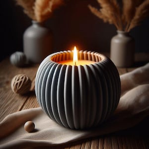 May include: A lit candle in a grey, ribbed ceramic holder. The candle sits on a beige cloth, with decorative vases and spheres in the background. The candle flame glows brightly, creating a warm ambiance.