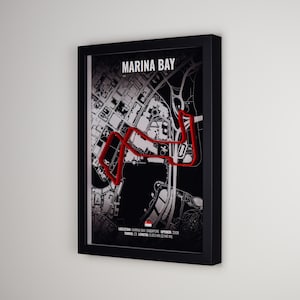 Peut inclure: Une œuvre d'art murale encadrée présentant une carte en noir et blanc du circuit urbain de Marina Bay à Singapour. Une ligne rouge audacieuse trace le tracé du circuit sur la carte. Le texte indique MARINA BAY, 23 virages et 5,063 km de longueur.