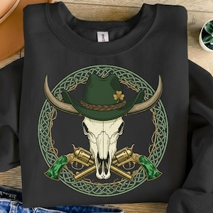 Puede incluir: Sudadera negra con un gráfico de una calavera de toro con un sombrero de vaquero verde con un trébol, revólveres dorados cruzados y un diseño de nudo celta verde. El diseño está centrado en la parte delantera de la camisa.