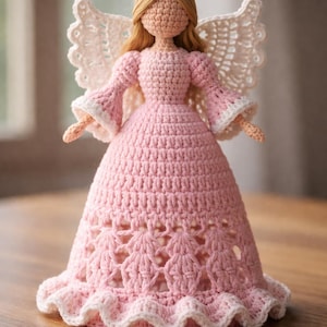 May include: A handmade crochet angel doll in a pink dress with white trim. The doll has blonde hair, a gold halo, and white wings. The dress features a detailed openwork design. The angel is a decorative item.
