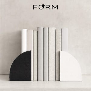 Könnte beinhalten: Minimalistische Komposition mit einer Reihe von Büchern in verschiedenen Weiß- und Grautönen, flankiert von einem schwarzen und einem weißen halbkreisförmigen Buchstützen. Das Wort "FORM" ist schwarz dargestellt, zentriert oben.