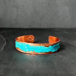May include: A copper bracelet with a turquoise inlay. The bracelet is hammered and has a rough, textured surface.