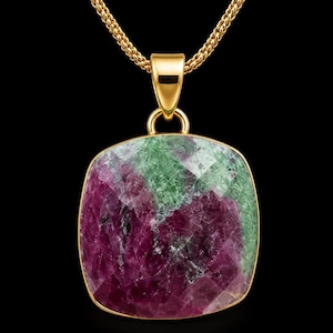 Könnte beinhalten: Eine Goldhalskette mit einem großen, quadratischen, facettierten Edelstein in den Farben tiefes Magenta und Waldgrün. Der Stein ist in einen Goldrahmen gefasst und an einer polierten Goldöse befestigt, die mit einer passenden Goldkette verbunden ist.