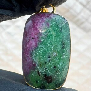 Può includere: Un ciondolo rettangolare con una pietra preziosa naturale di rubino e zoisite dalla superficie lucida. La pietra presenta un mix vibrante di magenta rosato intenso e verde bosco screziato con inclusioni scure, incastonato in una cornice dorata.
