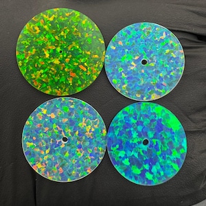 May include: Four circular opal cabochons in green and blue hues. Each has a small central hole. The opals display a mosaic pattern of colour and are set against a dark backdrop. The cabochons are likely for jewellery making.
