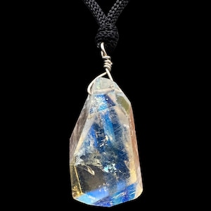 May include: A clear, irregularly shaped crystal pendant suspended from a black braided cord. The crystal features internal fractures and facets that reflect blue and yellow light, secured at the top by a silver-toned wire wrap.