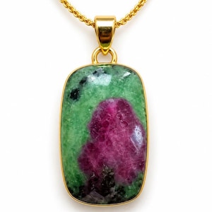 Puede incluir: Un colgante rectangular con una piedra preciosa de rubí zoisita pulida con inclusiones de color verde vibrante y magenta intenso, engastado en un marco de metal dorado liso, suspendido de una cadena de collar de metal dorado a juego.