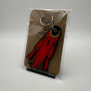 May include: A red and black keychain with a unique design, attached to a silver keyring. The keychain is packaged on a brown card with a logo that reads "NE3D". The design features a stylized shape with multiple details.