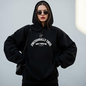 Peut inclure: Un sweat à capuche noir avec l'inscription blanche "Emotionally Tired, Don't Touch Me, Since Ever". Le sweat à capuche a une poche avant et une capuche. L'image montre une personne portant le sweat à capuche.