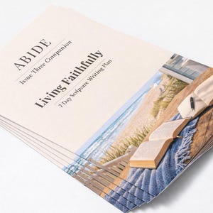 Peut inclure: Une pile de livrets imprim&eacute;s avec le titre "ABIDE" et "Living Faithfully". La couverture pr&eacute;sente une image d'un livre ouvert, d'un stylo et d'une sc&egrave;ne de plage. Les livrets sont empil&eacute;s sur une surface blanche.