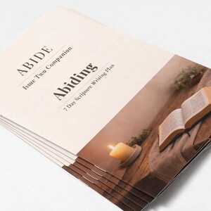 Peut inclure: Une pile de livrets cr&egrave;me avec le titre "ABIDE" et "Abiding" imprim&eacute;s en noir. La couverture pr&eacute;sente une image d'un livre ouvert, d'une bougie allum&eacute;e et de verdure sur une surface en bois. Les livrets sont pour un plan d'&eacute;criture de 7 jours.