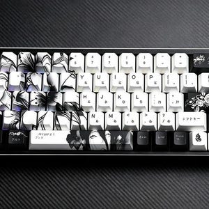 May include: A black and white mechanical keyboard with custom keycaps. The keycaps feature floral and anime-style designs, with Japanese characters. The keyboard has a black frame and a dark background.