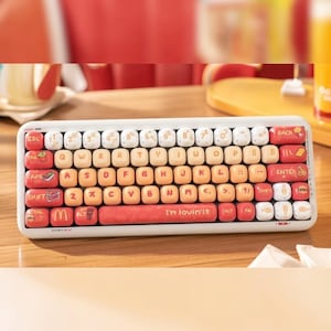 May include: A white and red mechanical keyboard with a fast food theme. The keys are a mix of white, orange, and red, with food-related icons and the phrase "I'm lovin'it" on the space bar. The keyboard is on a wooden surface.