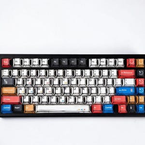 May include: A black mechanical keyboard with white and black keycaps. The keycaps have a unique design with a sketch-like aesthetic. The keyboard features a variety of colors on the keys, including red, blue, and orange.