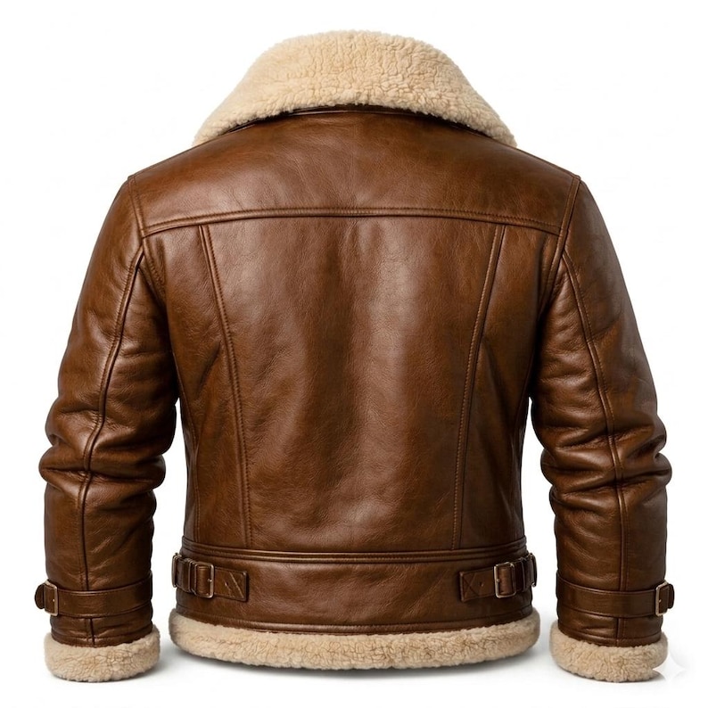 May include: A brown leather jacket featuring a thick cream-colored shearling collar and hem. The jacket includes long sleeves with adjustable buckle straps at the cuffs and a matching adjustable buckle strap detail along the back waistline.